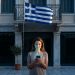 Shop owner in front of her closed shop on the morning of 28 October, checking her phone, with the Greek flag hanging from the balcony of a neoclassical building