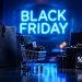 Φωτεινή επιγραφή Black Friday πάνω από μαύρες τσάντες αγορών, κουτιά δώρων με ετικέτες έκπτωσης και μικρό καρότσι αγορών